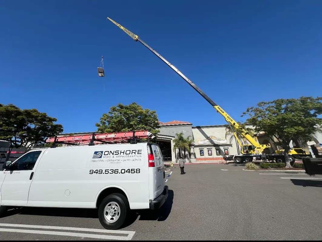 Onshore van and crane lifting rooftop HVAC unit onto commercial building